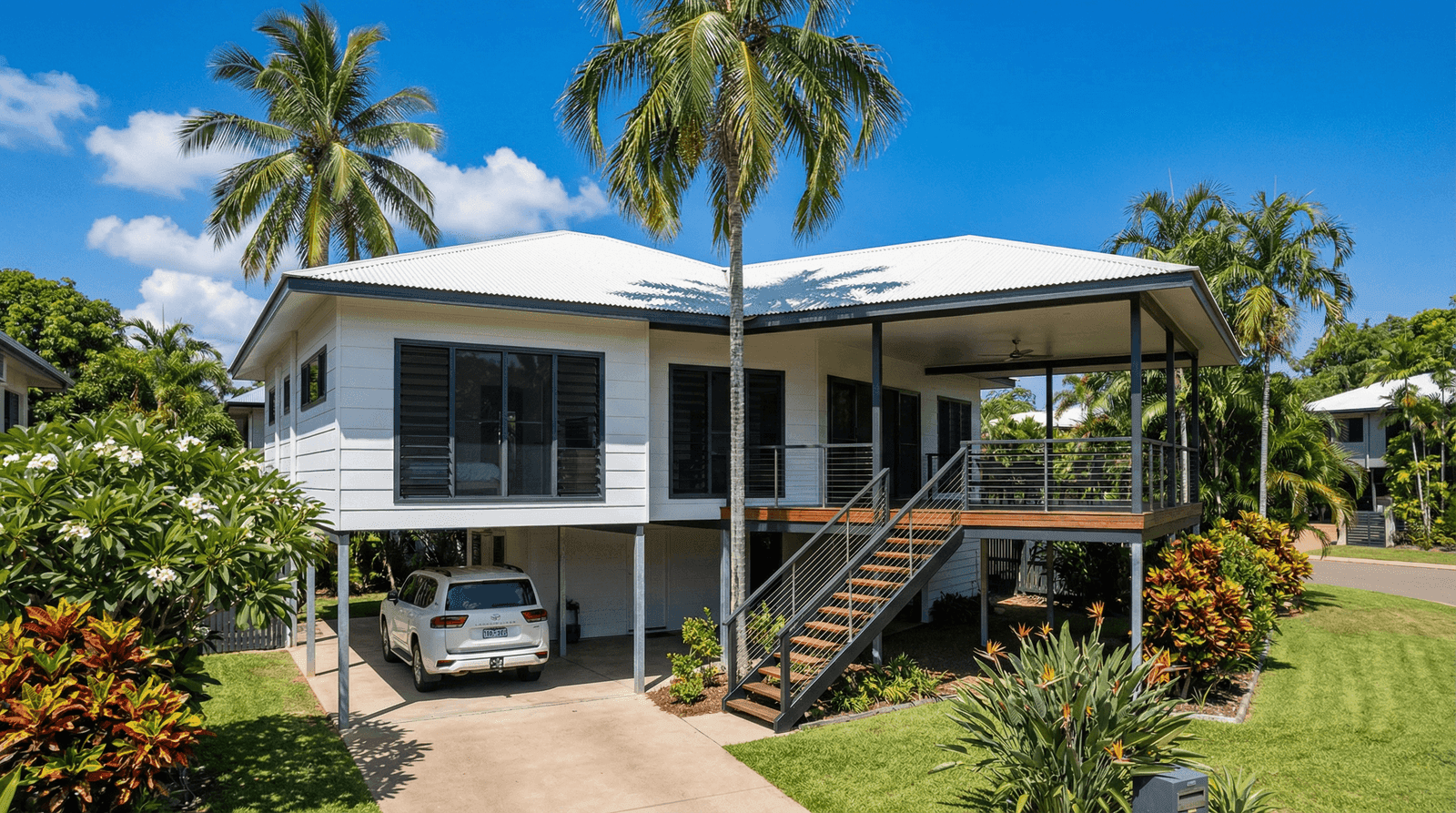 Newly completed modern elevated residential home in a Darwin suburb with Colorbond roof, louvre windows, hardwood stairs, and lush tropical landscaping including palm trees and frangipani