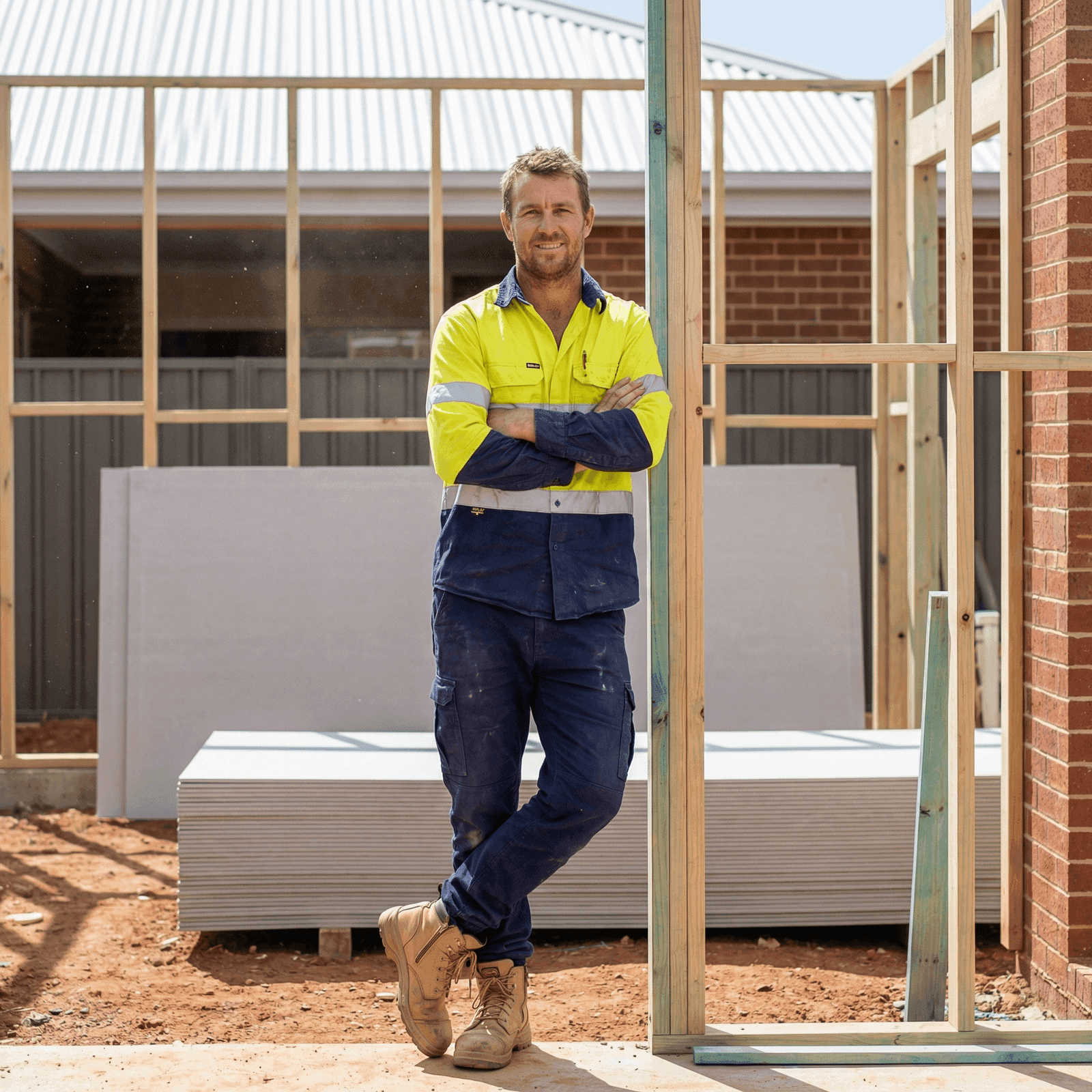 Experienced Australian builder standing confidently at a residential construction site with timber framing and brick veneer — RPL recognises this hands-on experience